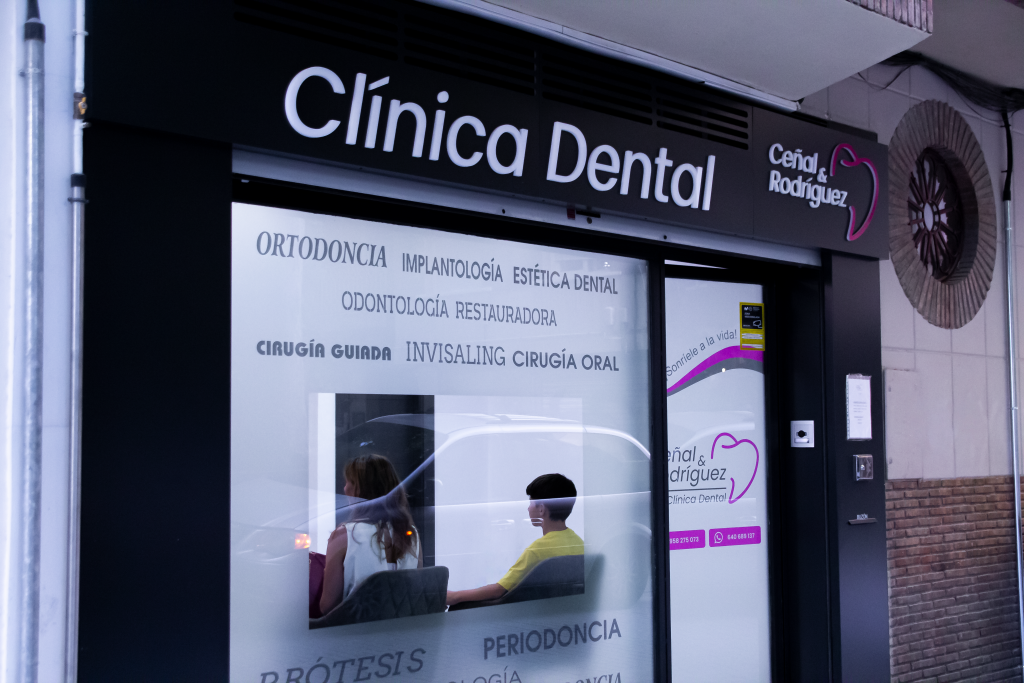 Entrada de Ceñal & Rodríguez Clínica Dental con diseño moderno, mostrando servicios como ortodoncia, implantología y estética dental en Granada centro.