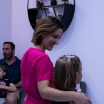 Dentista con uniforme rosa acompañando a una niña en una sala moderna, representando el trato cercano y profesional ofrecido por un dentista en Granada centro.