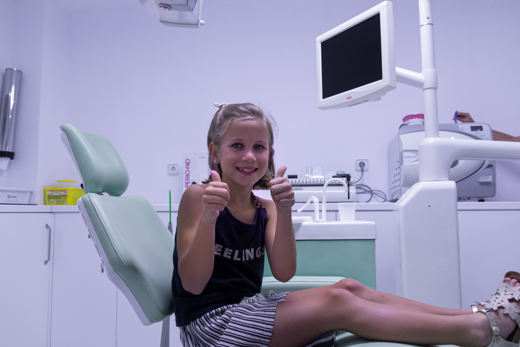 Niña sonriente levantando los pulgares mientras está sentada en un sillón dental, representando la atención cercana y profesional ofrecida por un dentista en Granada centro.