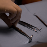 Mano con guante quirúrgico manipulando instrumentos odontológicos sobre una superficie azul, destacando la precisión y profesionalidad en los tratamientos realizados en Granada centro.