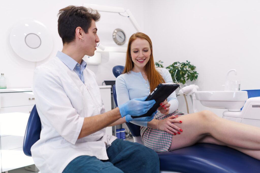 Dentista explicando a una paciente las aplicaciones y opciones de tratamiento disponibles, utilizando una tablet en un entorno clínico moderno.