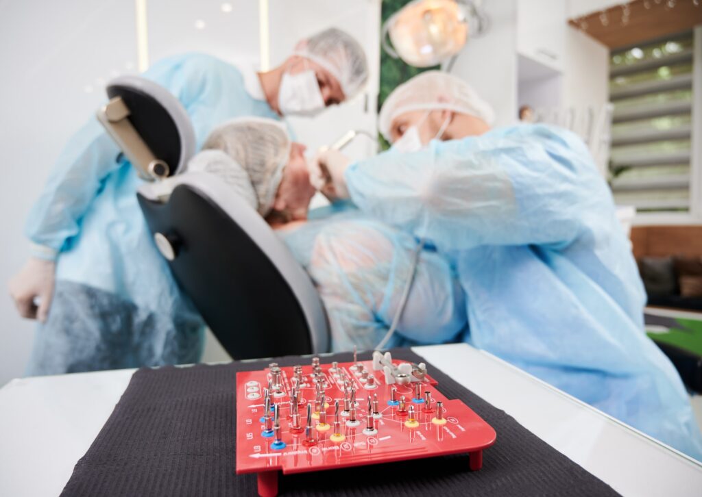 Kit de implantes dentales sobre una mesa en un consultorio dental, mientras dos profesionales realizan un procedimiento. Representa la importancia de recomendaciones y decisiones informadas en tratamientos odontológicos.