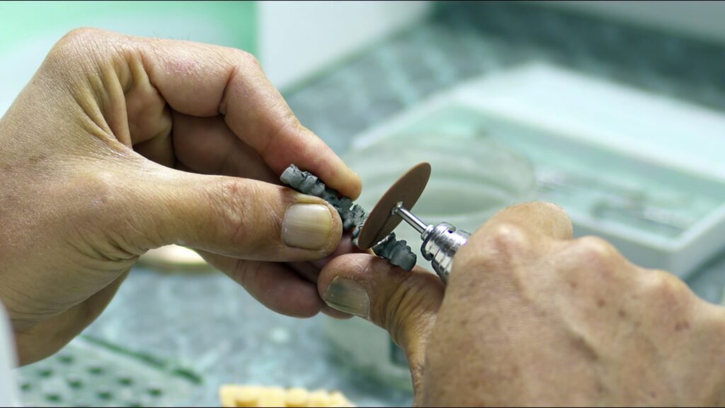 Primer plano de un técnico dental trabajando en la fabricación de implantes de zirconio, utilizando herramientas de precisión para dar forma al material.