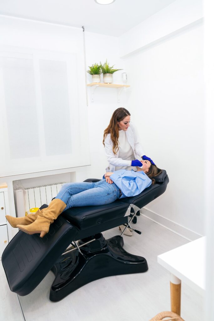 Imagen de una profesional atendiendo a una paciente recostada en una camilla en una clínica. Representa los cuidados y consejos post tratamiento para garantizar una recuperación adecuada y óptimos resultados.
