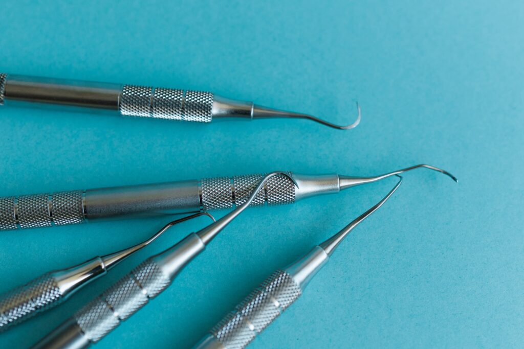 Primer plano de varios raspadores periodontales metálicos sobre un fondo azul, utilizados en la prevención de la periodontitis y el cuidado dental profesional.