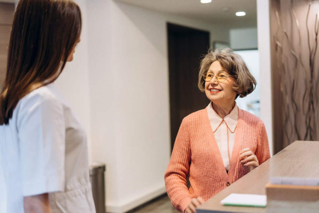 Imagen de una paciente hablando con la recepcionista en una clínica dental. Representa el proceso de comparación de precios en diferentes clínicas para tratamientos como empastes dentales.