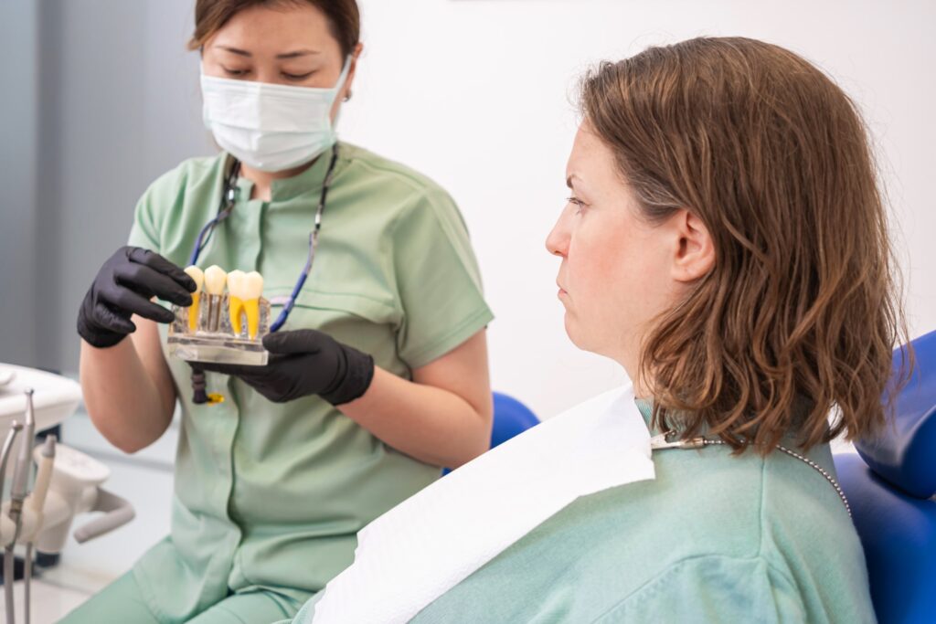 Dentista mostrando un modelo de dientes a un paciente en consulta, destacando los hábitos a evitar tras la cirugía para garantizar una recuperación adecuada.