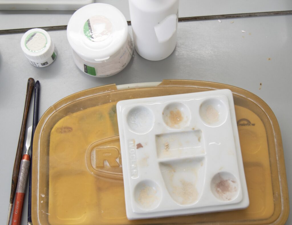 Utensilios y materiales dentales ordenados sobre una mesa de clínica, listos para ser utilizados durante los cuidados inmediatos postoperatorios, incluyendo una paleta de mezclas, pinceles y frascos de productos odontológicos.