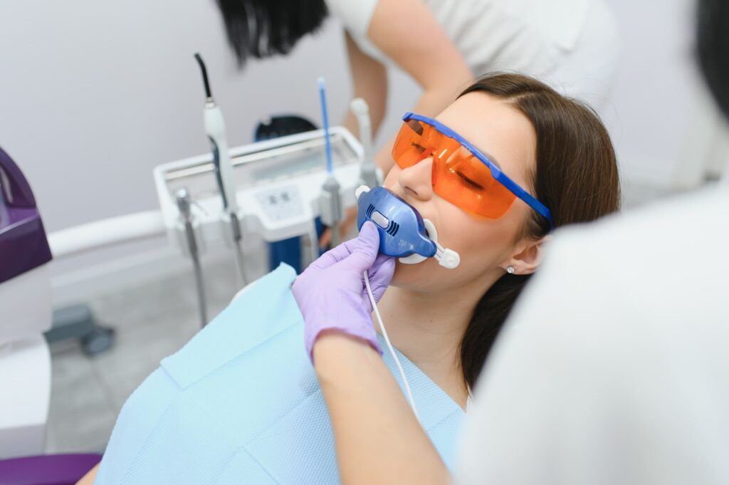 Paciente recibiendo un blanqueamiento dental profesional con luz LED en la clínica Ceñal & Rodríguez, usando gafas protectoras y supervisada por un odontólogo especializado, destacando la tecnología avanzada y el cuidado personalizado en blanqueamientos dentales. Palabra clave: La clínica Ceñal & Rodríguez y su oferta en blanqueamientos dentales.