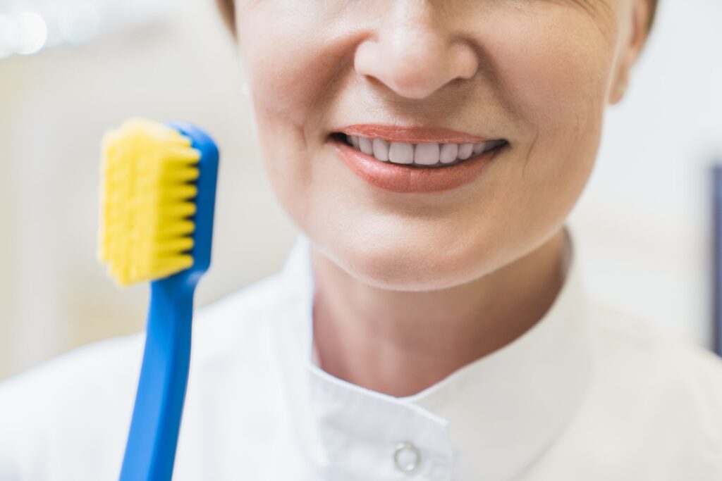 Primer plano de una persona sonriendo con dientes blancos mientras sostiene un cepillo de dientes amarillo, representando la importancia de la higiene bucal en el cuidado de las carillas dentales y desmintiendo mitos comunes sobre su mantenimiento.