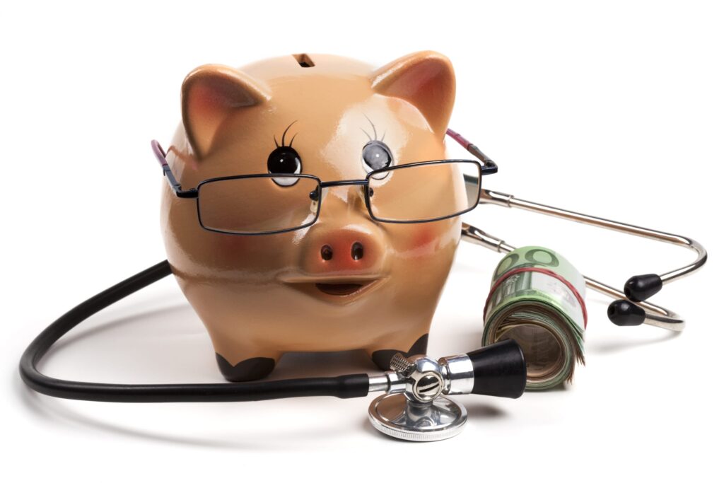 Hucha en forma de cerdito con gafas, acompañada de un estetoscopio y un fajo de billetes, simbolizando opciones de financiación y gestión de costes para tratamientos odontológicos.