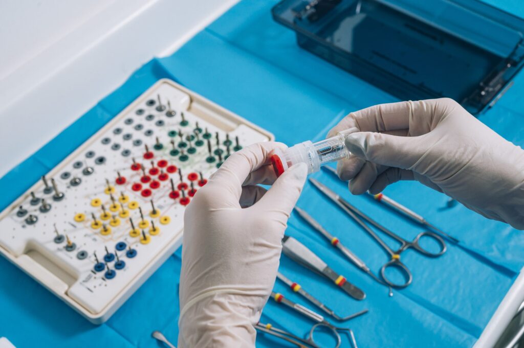 Manos con guantes sosteniendo un implante dental junto a un kit de herramientas odontológicas sobre una superficie azul. La imagen representa el proceso y los materiales utilizados en procedimientos de implantes dentales, ideal para abordar dudas frecuentes del postoperatorio.