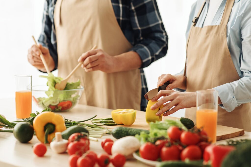 Personas preparando una ensalada con vegetales frescos como pimientos, tomates y pepinos, ideal para una dieta equilibrada en la alimentación postoperatoria.
