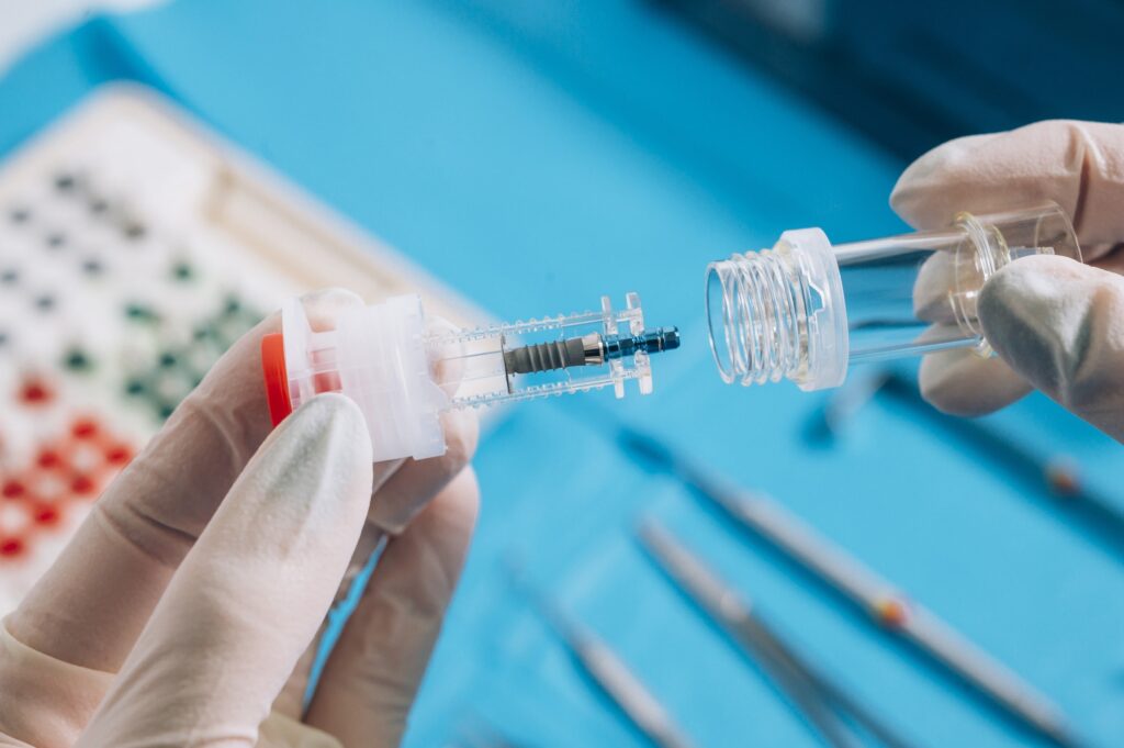 Manos enguantadas manipulando un implante dental en un entorno clínico, ilustrando la importancia de conocer las posibles complicaciones y cómo actuar tras el procedimiento.