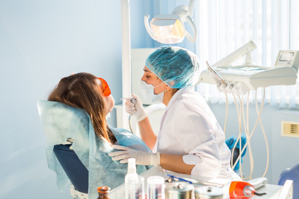 Dentista realiza un tratamiento de blanqueamiento dental a una paciente en el consultorio, mostrando el equipo odontológico y el uso de gafas protectoras.