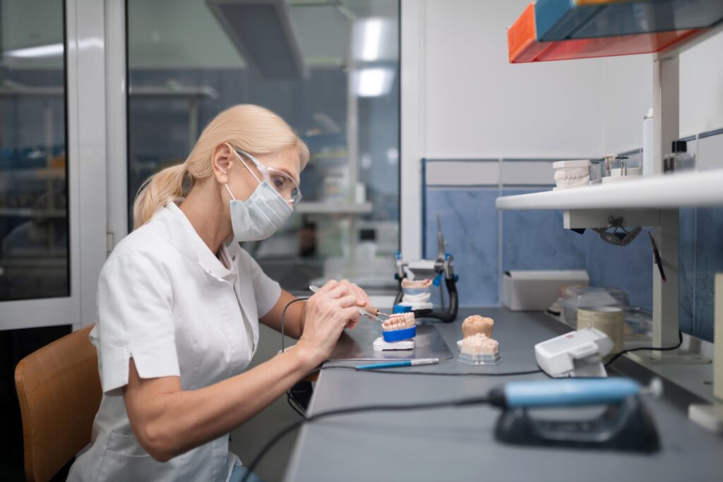 Técnico dental en laboratorio diseñando y ajustando carillas dentales sobre un modelo dental, mostrando el proceso de creación de diferentes tipos de carillas dentales.