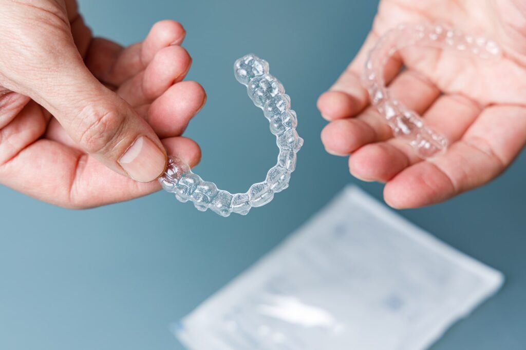 Primer plano de unas manos sosteniendo alineadores transparentes Invisalign, resaltando la diferencia visual y funcional entre Invisalign y otros sistemas de ortodoncia tradicionales.