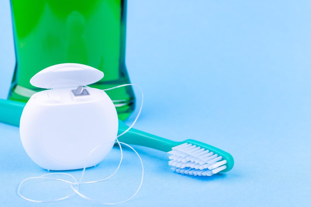 Imagen de hilo dental, cepillo de dientes y enjuague bucal sobre fondo azul, representando los cuidados después de un empaste dental.