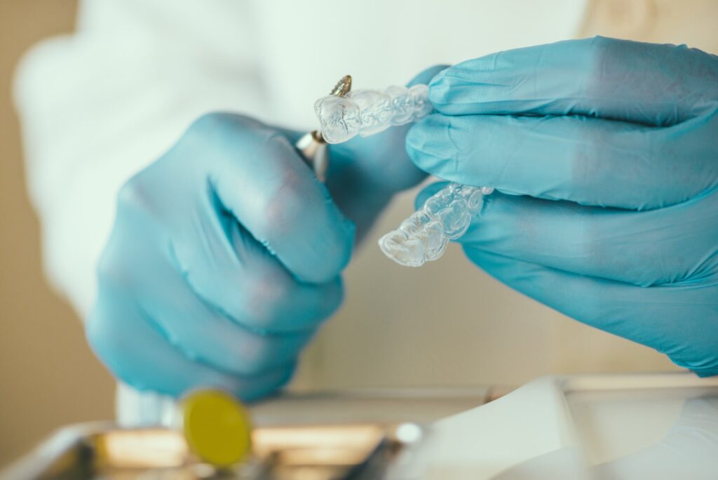 Primer plano de un dentista con guantes azules ajustando un alineador transparente Invisalign en la clínica, destacando la experiencia y profesionalismo de nuestra clínica en el tratamiento de Invisalign.