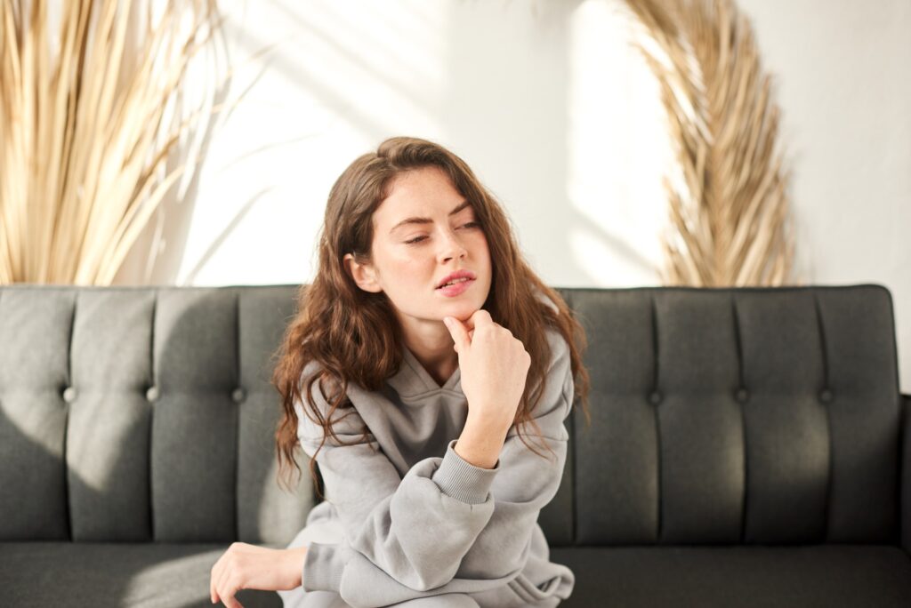 Mujer pensativa sentada en un sofá, evaluando las ventajas y desventajas del tratamiento con Invisalign, ideal para ilustrar la toma de decisiones antes de elegir este método de ortodoncia.