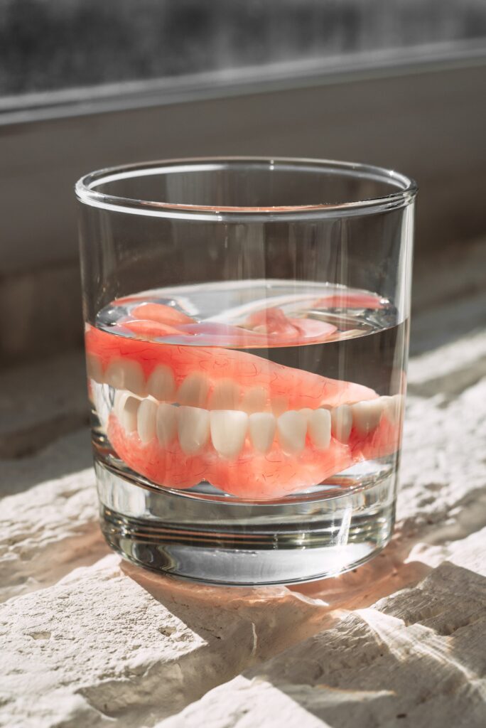 Prótesis dental tradicional sumergida en un vaso con agua, ilustrando la diferencia entre dentaduras removibles y otras soluciones dentales modernas como los implantes.