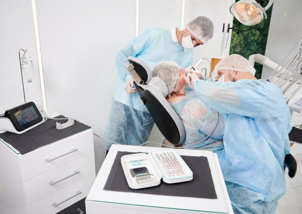 Cirujanos dentales realizando una intervención de implantes dentales en un consultorio equipado, mostrando instrumental específico de implantología, destacando el uso del titanio por su biocompatibilidad, resistencia y durabilidad en los tratamientos dentales.