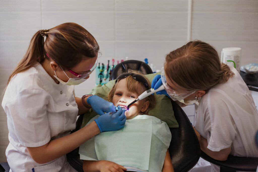 Dos dentistas realizan un procedimiento de empaste dental a un niño en una clínica, ilustrando la duración del procedimiento de empaste y el cuidado profesional durante el tratamiento.