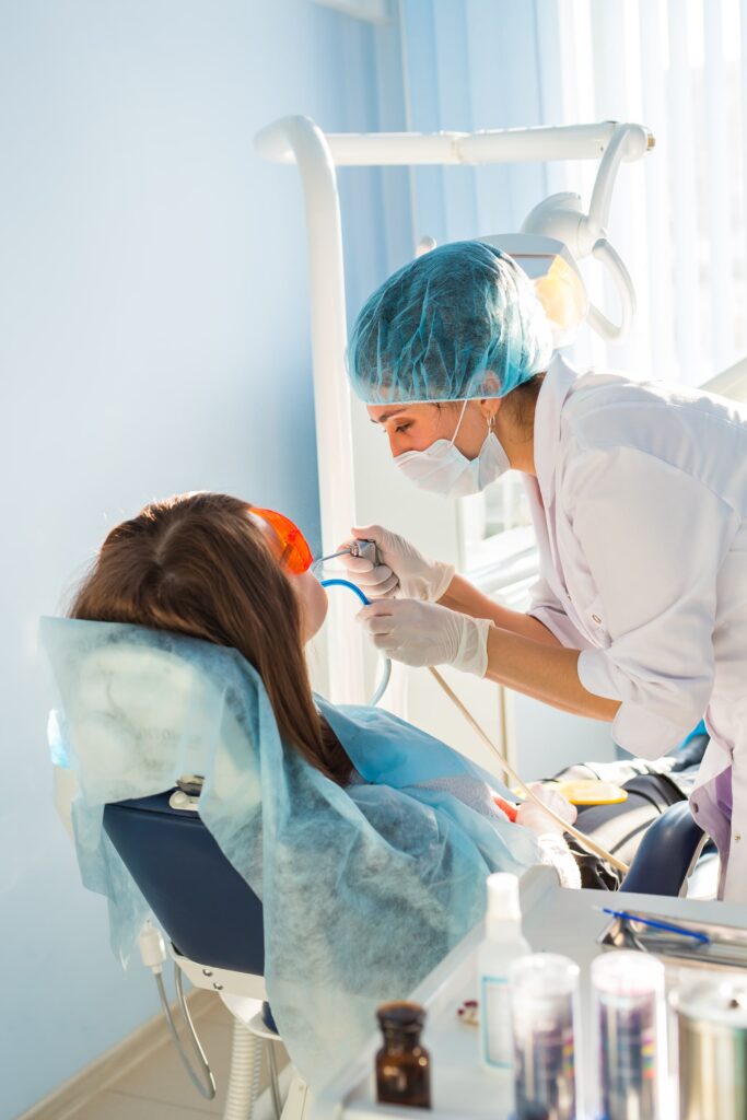 Dentista realizando un tratamiento dental profesional a una paciente en una clínica moderna, ilustrando los efectos rejuvenecedores de una sonrisa saludable y cuidada gracias a la atención odontológica especializada.
