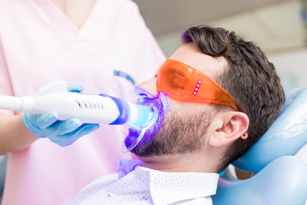 Dentista aplicando un tratamiento de blanqueamiento dental a un paciente en una clínica, representando los posibles efectos secundarios del blanqueamiento dental.