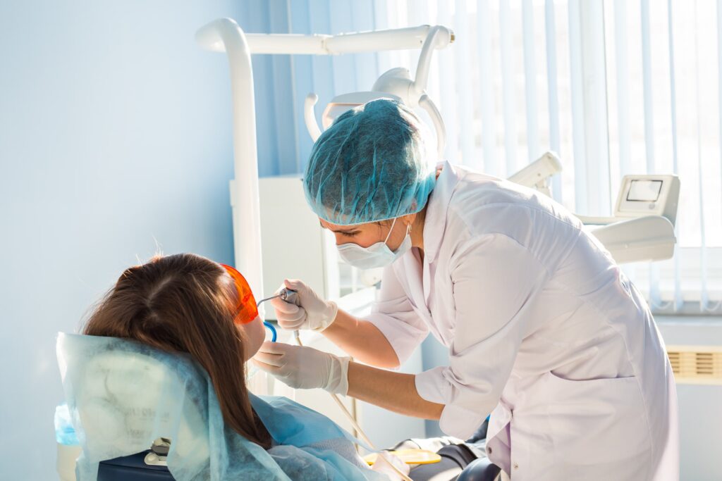 Dentista realizando un tratamiento estético dental a una paciente en una clínica moderna, ilustrando el contexto de las preguntas frecuentes sobre estética dental, como los procedimientos, cuidados y resultados esperados.