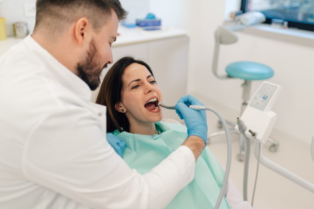 Odontólogo atendiendo a un paciente en una clínica moderna, ejemplificando las promociones actuales en implantes en Clínica Dental Ceñal & Rodríguez, con instrumental dental y ambiente profesional.