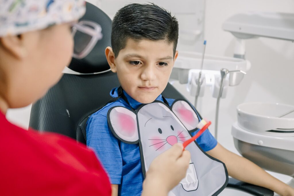 Dentista mostrando una técnica de cepillado a un niño en una consulta dental moderna, ejemplificando el enfoque de atención integral donde se explican los tipos de implantes y tratamientos relacionados para la salud bucal desde temprana edad.