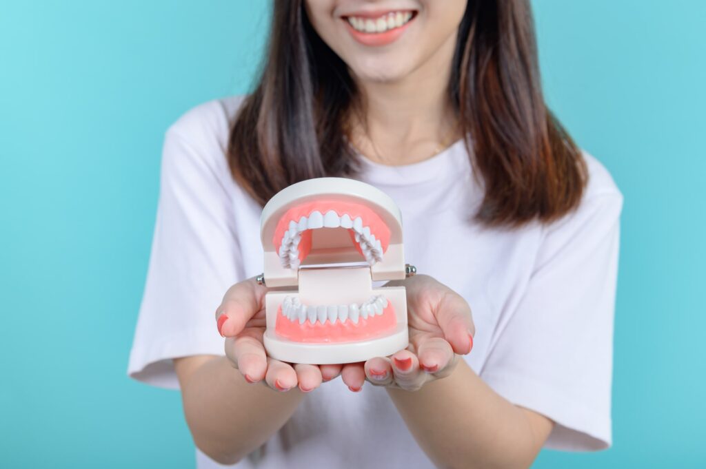 Mujer sonriente sostiene un modelo dental en sus manos, simbolizando la importancia de los cuidados después del tratamiento Invisalign para mantener los resultados y una sonrisa sana.