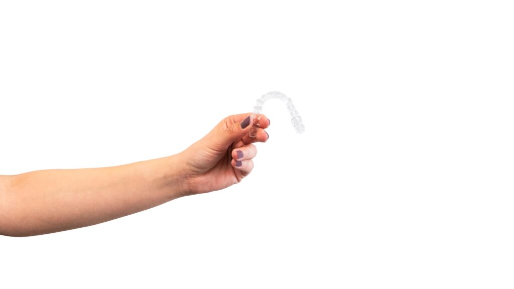Mano de mujer sosteniendo un alineador transparente sobre fondo blanco, representando las indicaciones y los problemas dentales que corrige Invisalign, como la alineación de los dientes y la corrección de maloclusiones.