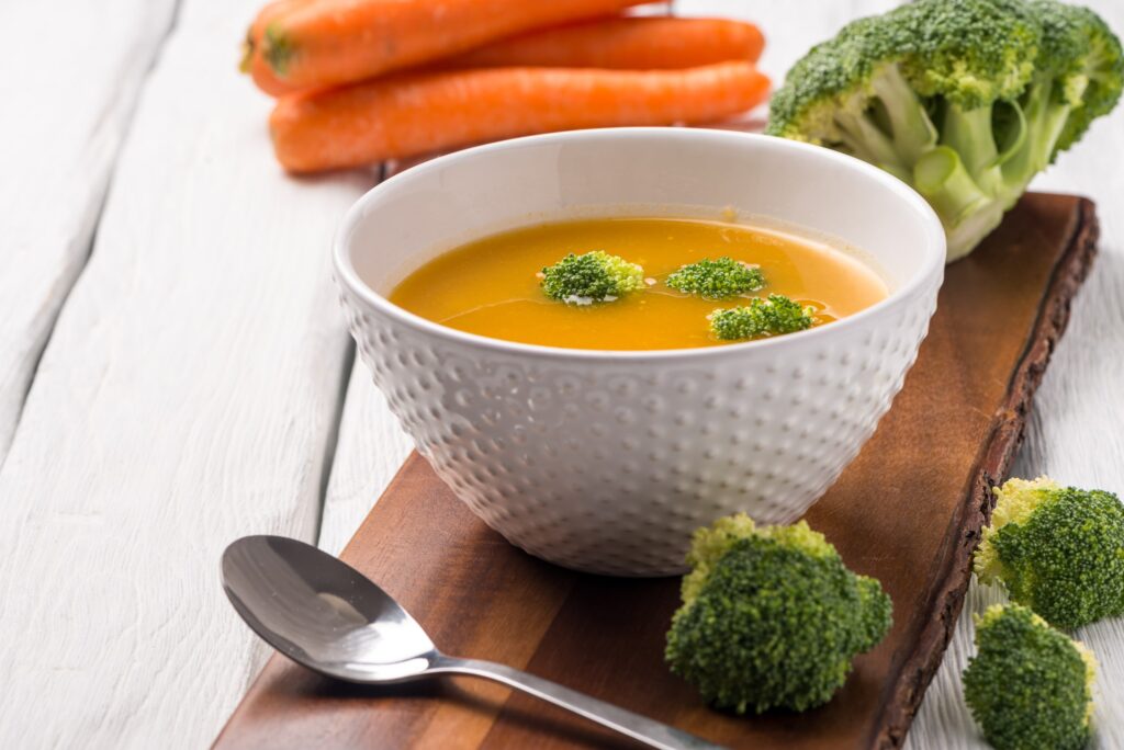 Plato de sopa de verduras suave acompañado de brócoli y zanahorias, ideal para la dieta durante los primeros días después de la intervención, facilitando la recuperación y evitando molestias.