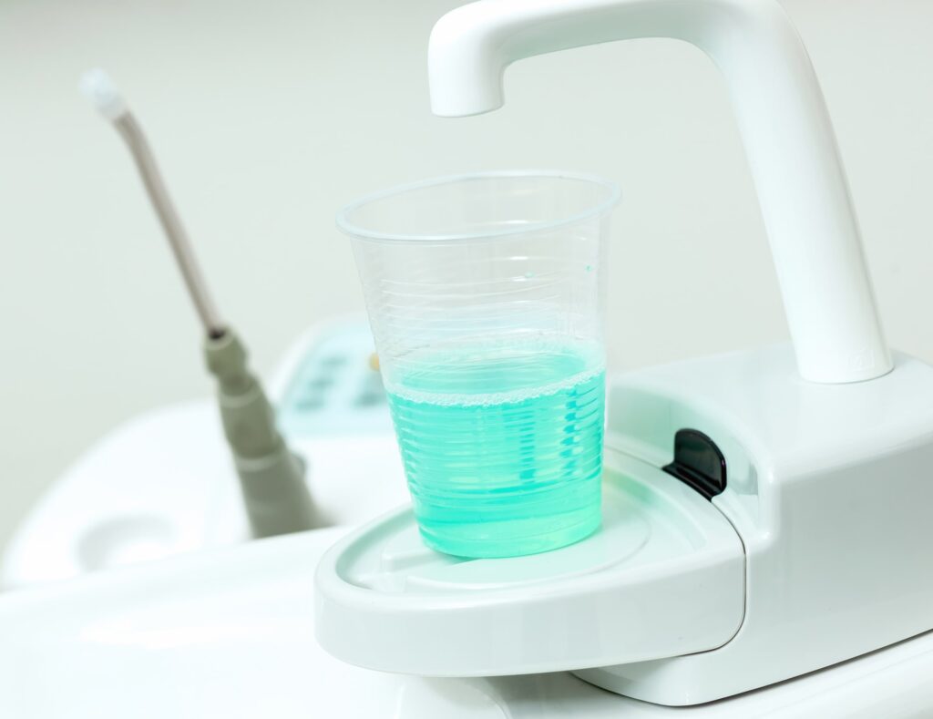 Imagen de un vaso con colutorio verde colocado en una unidad dental, representando el tratamiento con colutorio utilizado durante visitas odontológicas para mejorar la higiene bucal del paciente.