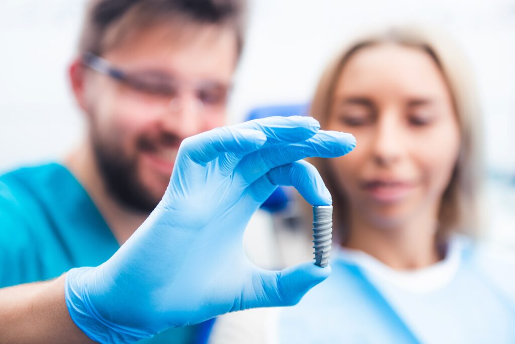 Odontólogo con guantes azules mostrando un implante dental de titanio frente a una paciente para explicar la durabilidad de los implantes dentales y su éxito a largo plazo.